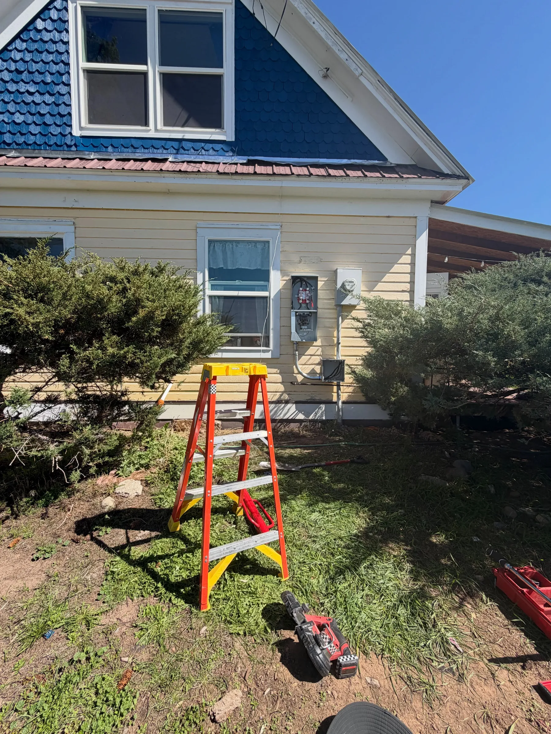 A ladder set up beside a blue-trimmed house during a panel service upgrade