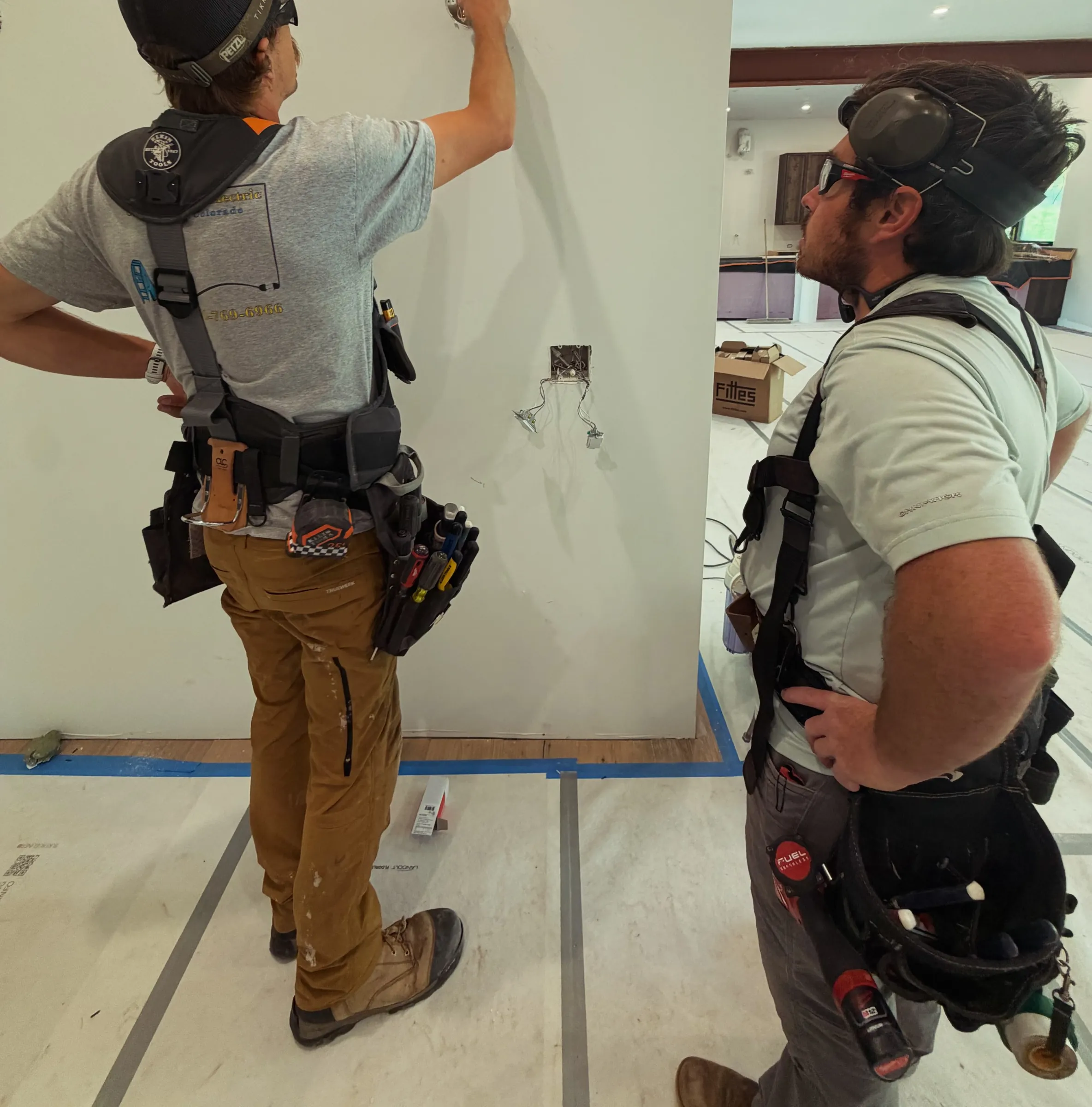 Two electricians in tool belts checking wiring in a new build