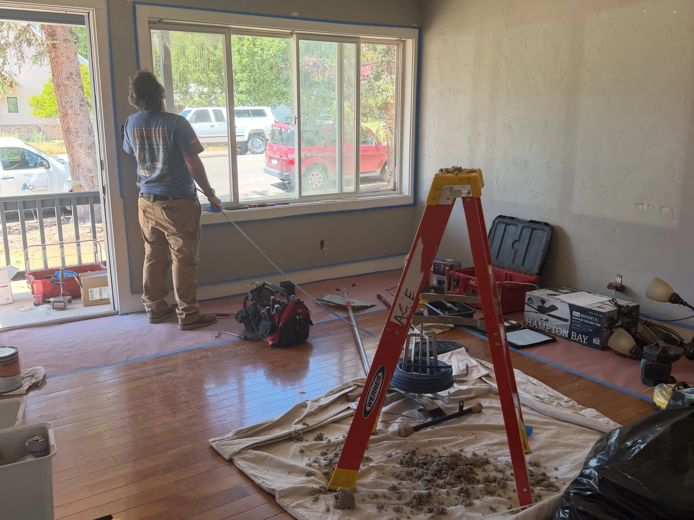 Rewiring underway in a living room during a remodel, with a ladder and tools on drop cloths