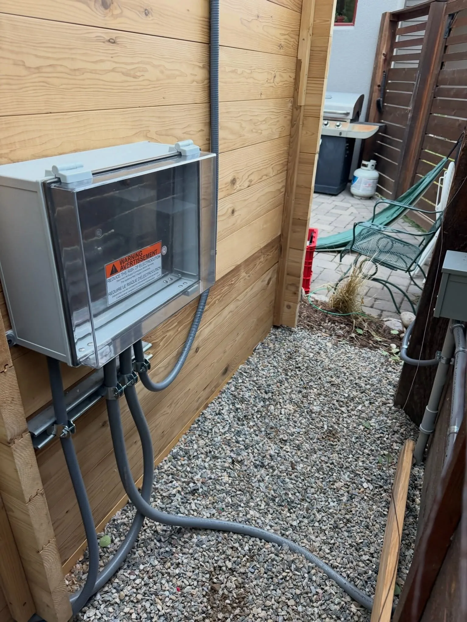 An outdoor electrical disconnect and conduit mounted beside a backyard sauna