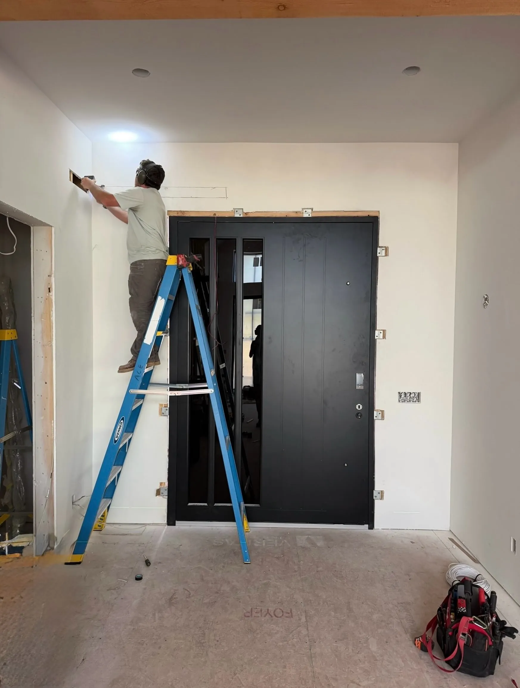 An electrician on a ladder adding power for a black high-security smart door